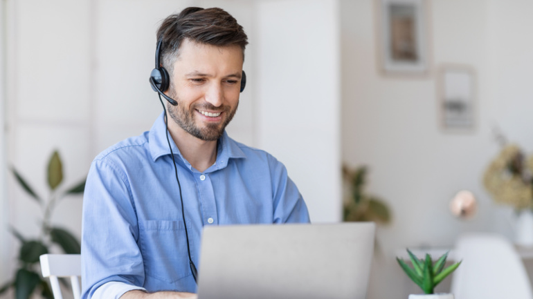 Call center operator at work. Positive male manager wearing headset using unified communications software
