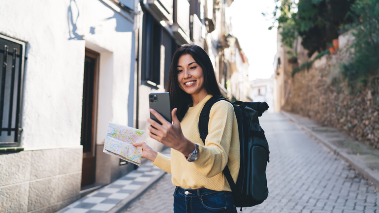 Joyful female tourist enjoying solo vacations using location map during travel sightseeing in touristic village, happy hipster girl connecting to roaming internet for making online video vlog