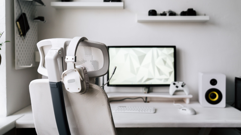 White large gaming headphones with a microphone hang on a white armchair. Cloud gaming.