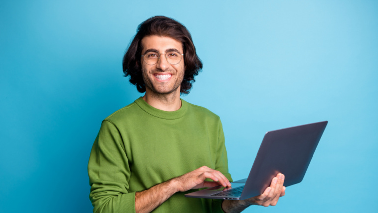 A quick roundup of the news in Telecoms | Week #24, Photo of cheerful programmer guy hold netbook look camera wear glasses green pullover isolated blue color background