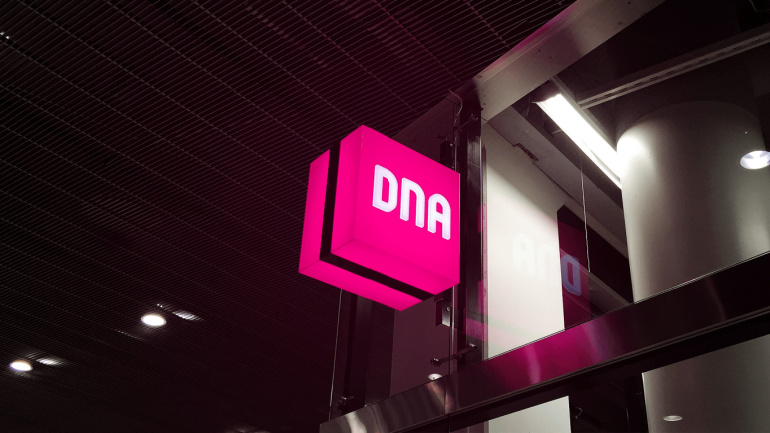 DNA Finland providers company logo outside the building in the night, bright pink logo with white DNA letters glowing in the dark